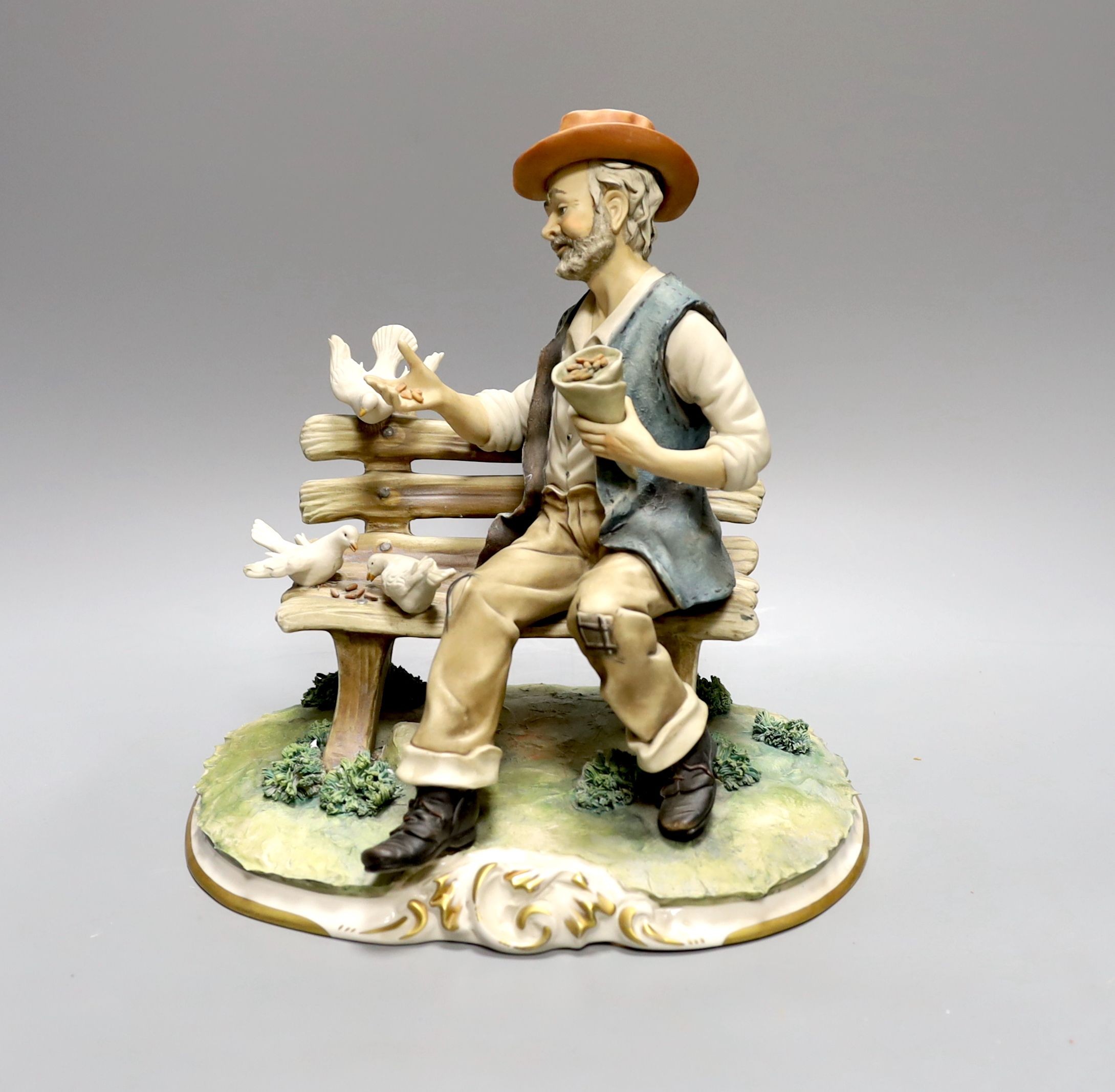 A Capodimonte figure of a tramp sat on a bench feeding doves 27cm